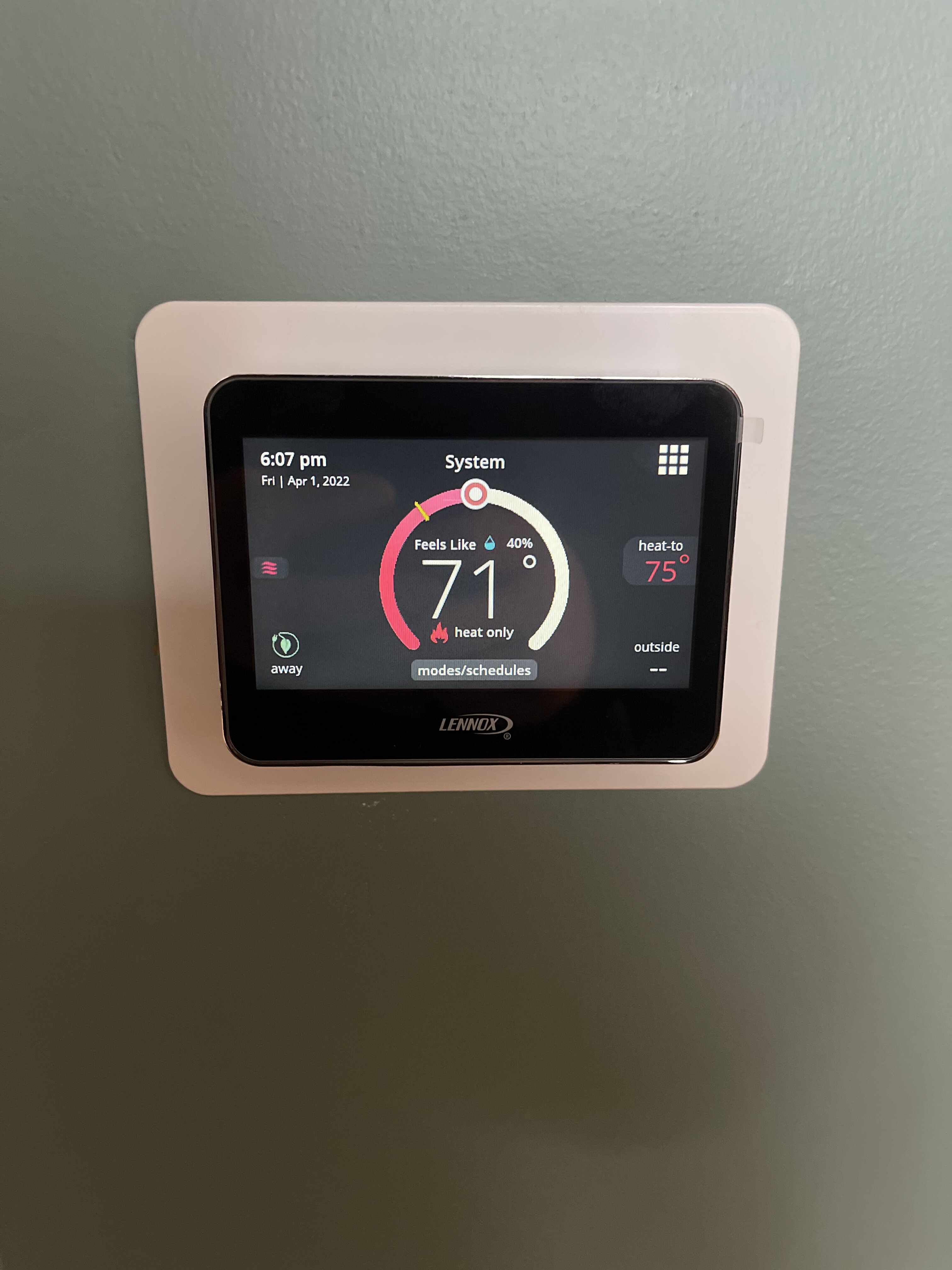 A wall thermostat showing indoor temperature and humidity